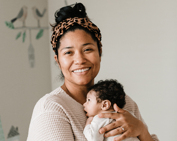 Smiling woman wearing a leopard print headband holding a newborn baby close to her chest.