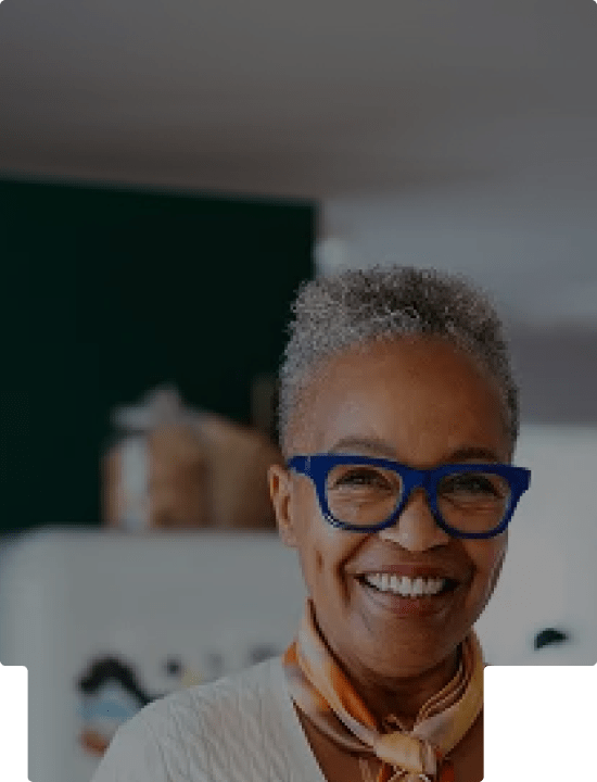 Smiling older woman with short gray hair, wearing blue glasses and a light scarf.
