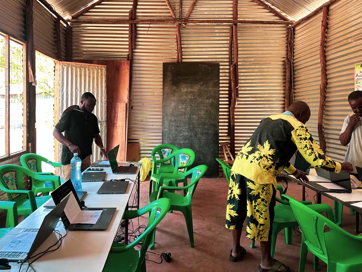 Young people at laptops on long tables with green chairs