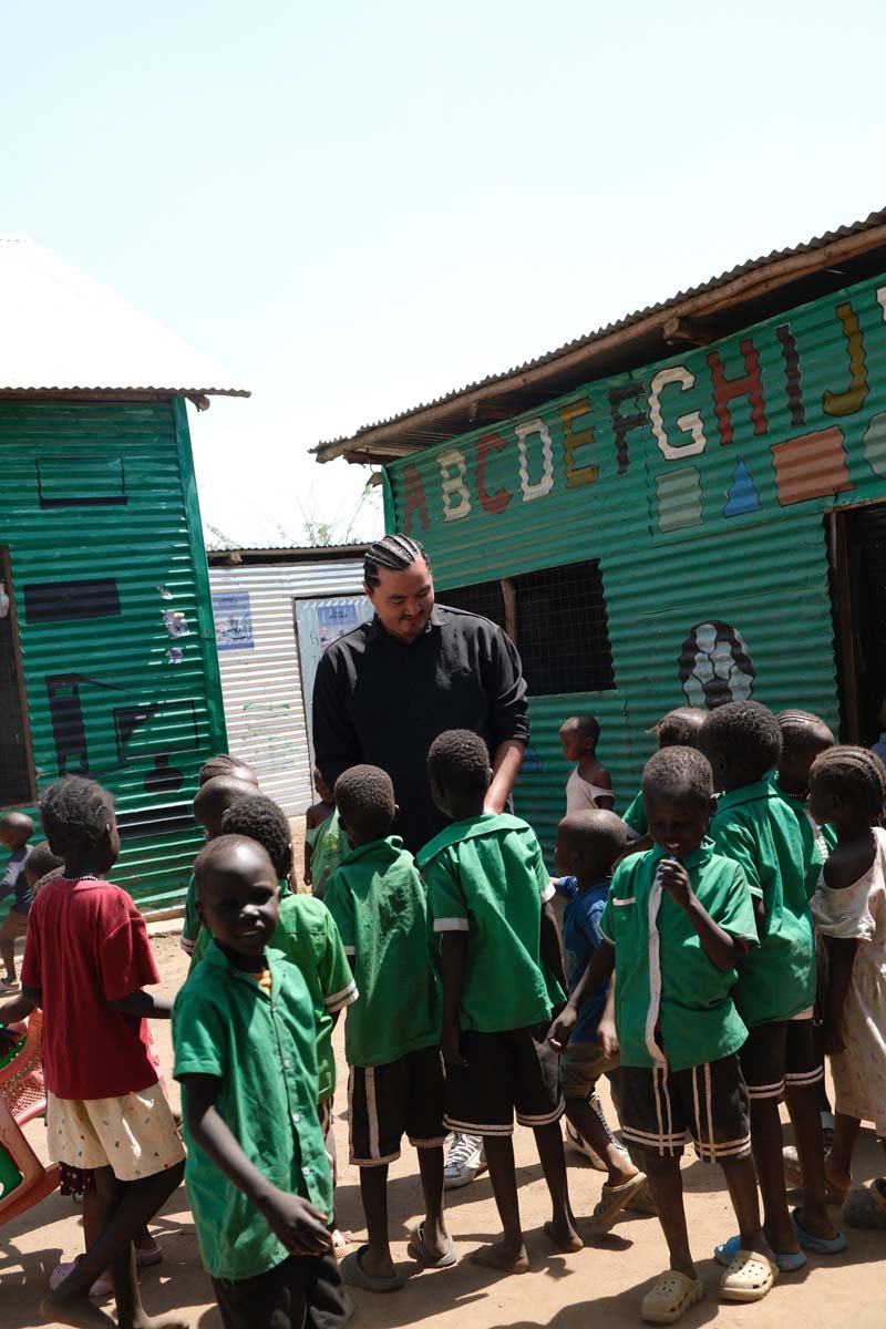 Children in green school uniforms outside green buildings in Kakuma