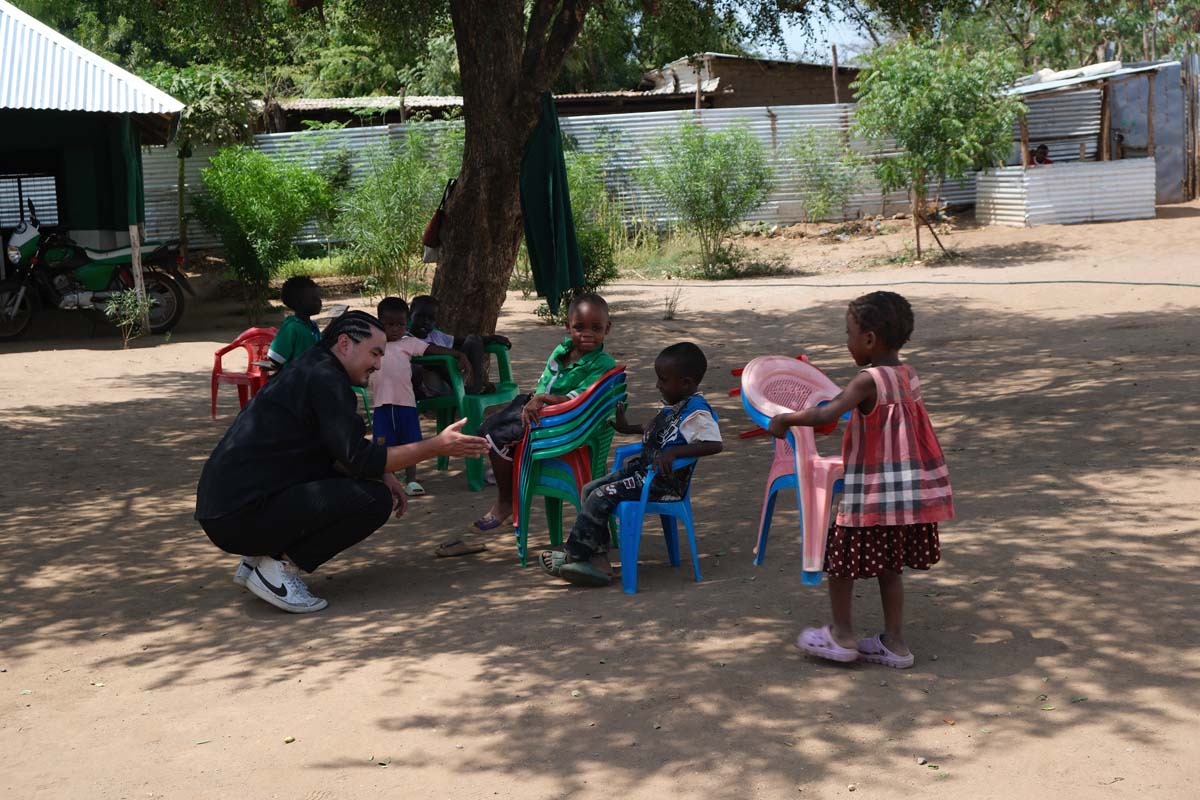 Crouching with young children in the shade of a tree in Kakuma