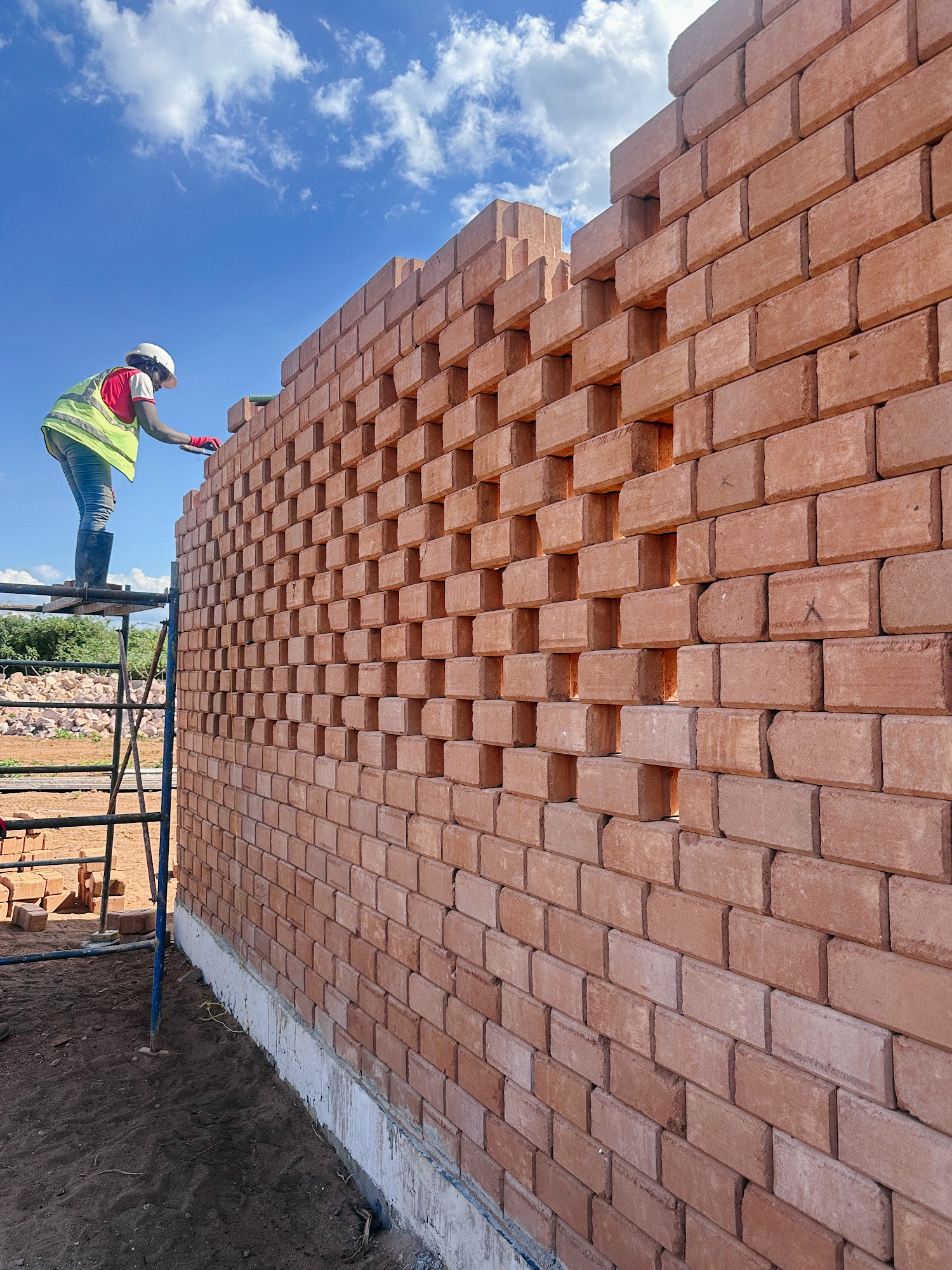 A builder in a hard hat and high-visibility vest laying bricks from a scaffold