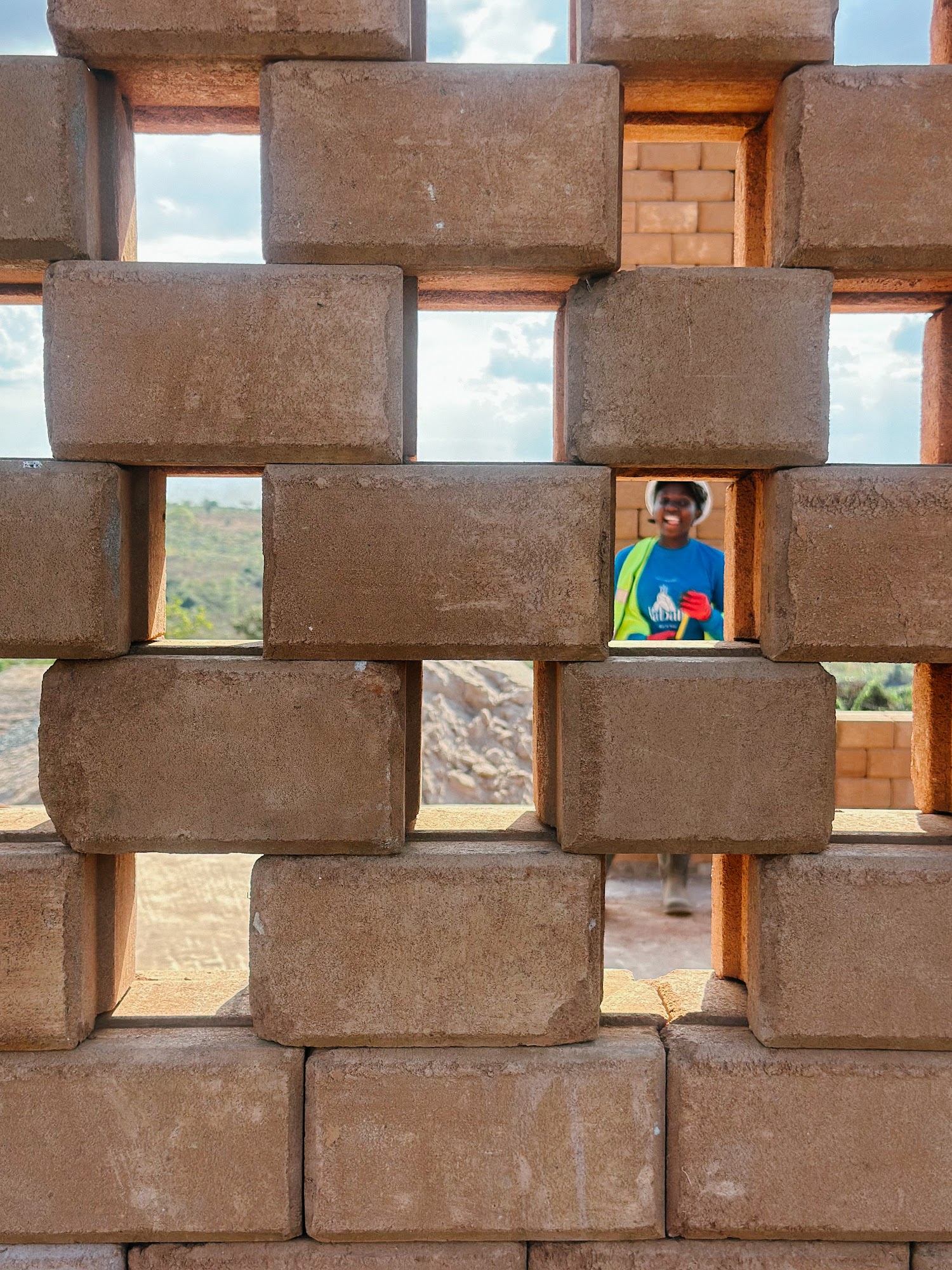 A smiling builder seen through the gaps of a perforated brick wall