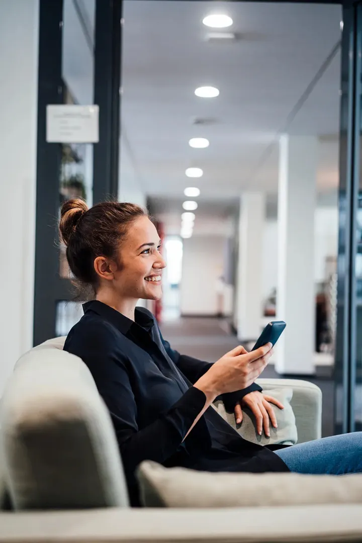 Frau entspannt mit Smartphone in moderner Büro-Lounge – Symbolbild für digitale Kommunikation und Zufriedenheit mit den Lösungen von Haufe.