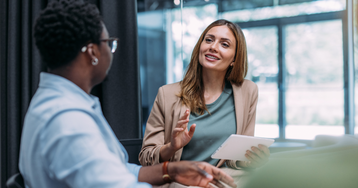 Zwei Personen besprechen sich im modernen Büro, eine davon hält ein Tablet in der Hand. Sie tauschen sich über digitale Lösungen für HR aus