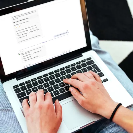 Hände tippen auf einer Laptop-Tastatur, während ein Chat-Interface den CoPilot HR von Haufe auf dem Bildschirm angezeigt.
