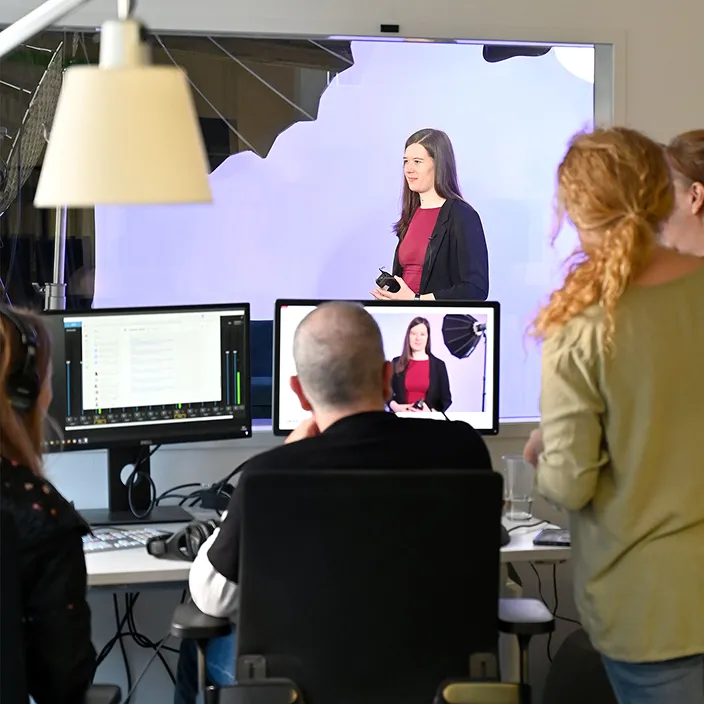 Drei Personen beobachten am Schreibtisch einen Monitor, der Julia Senner bei Videoaufnahmen für die HR-Online-Konferenz 2026 zeigt.