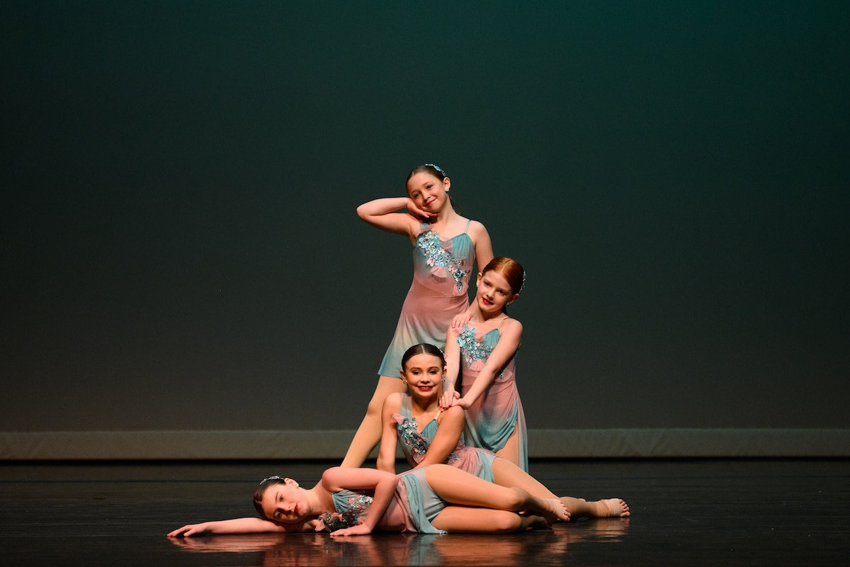 Dancers in teal and pink outfits pose on stage