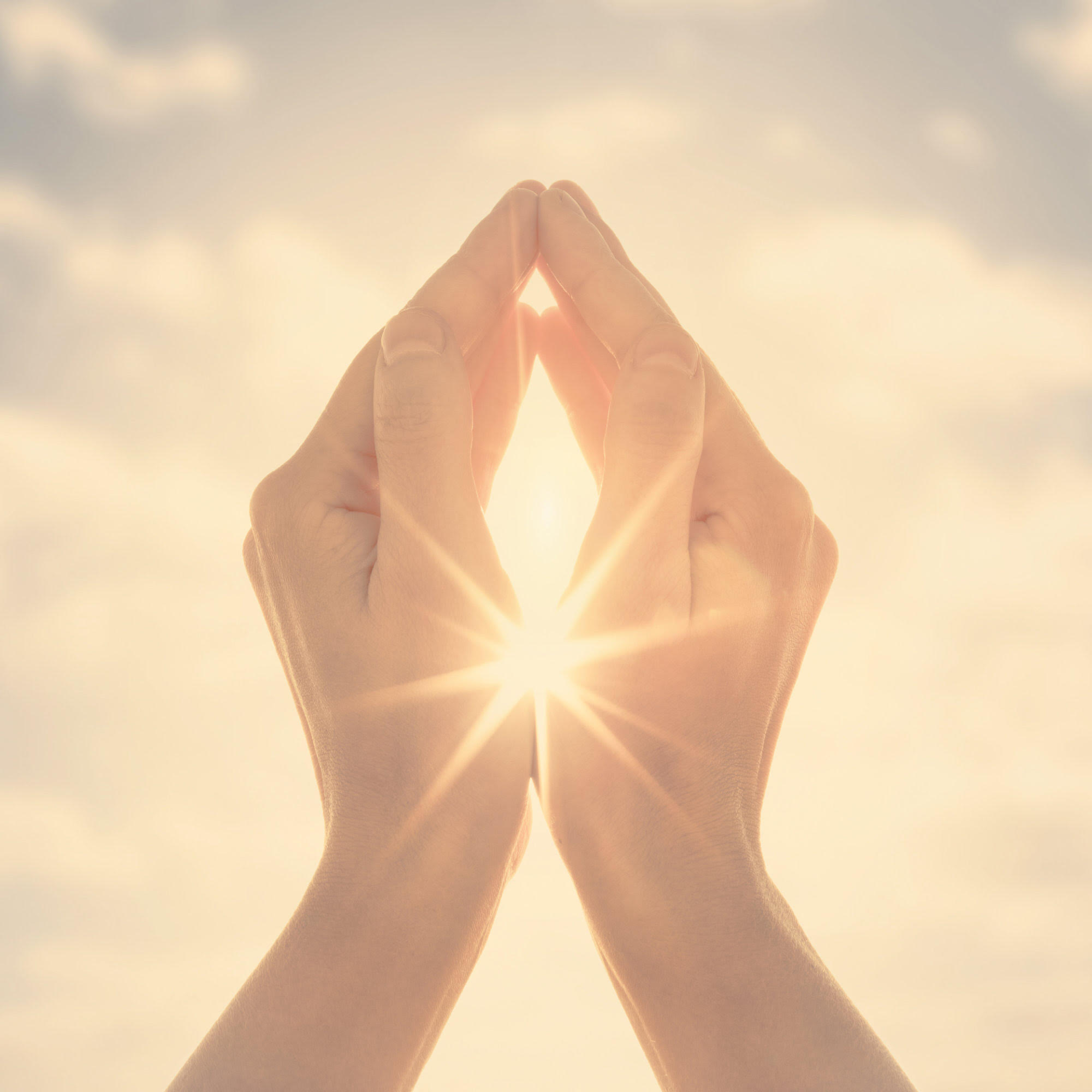Zwei Hände, die sich mit den Fingerspitzen berühren und durch deren Mitte Sonnenlicht strahlt.