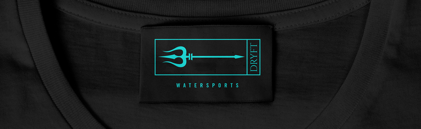 Black shirt label with a turquoise trident logo and text reading 'DRYFT' and 'WATERSPORTS'.