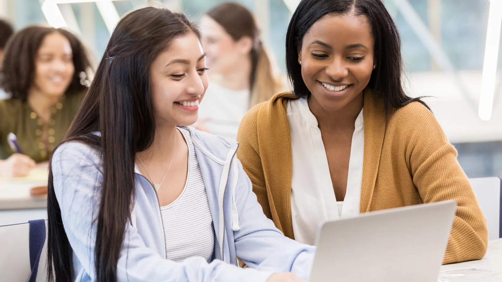 Two women are smiling while looking at a laptop. - ASSISTments Images