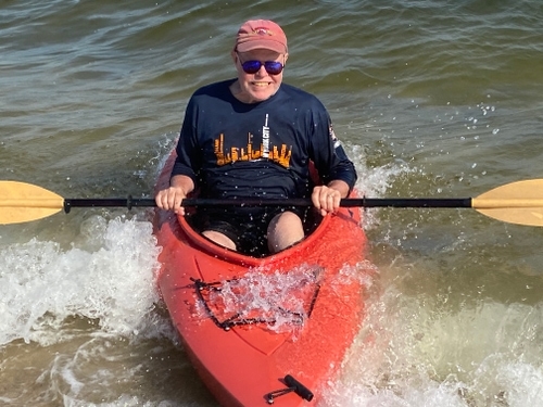 Kenneth riding in a kayak sporting sunglasses and smiling as the water crashes around him.