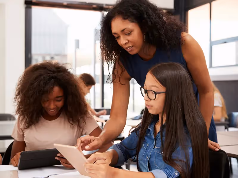 A woman teaching a class of young girls how to use a tablet.