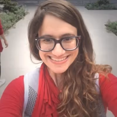 A woman wearing a red shirt, glasses and a backpack smiling. - Assistments - Formative Assessment Solutions