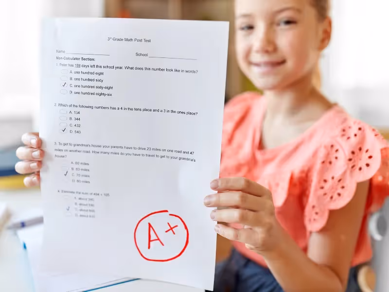 A girl holding a piece of paper with a red A+ on it. - ASSISTments Images