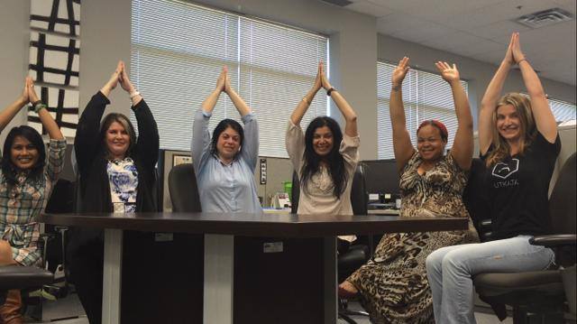 Participants in work clothes following a seated stretch in a meeting room