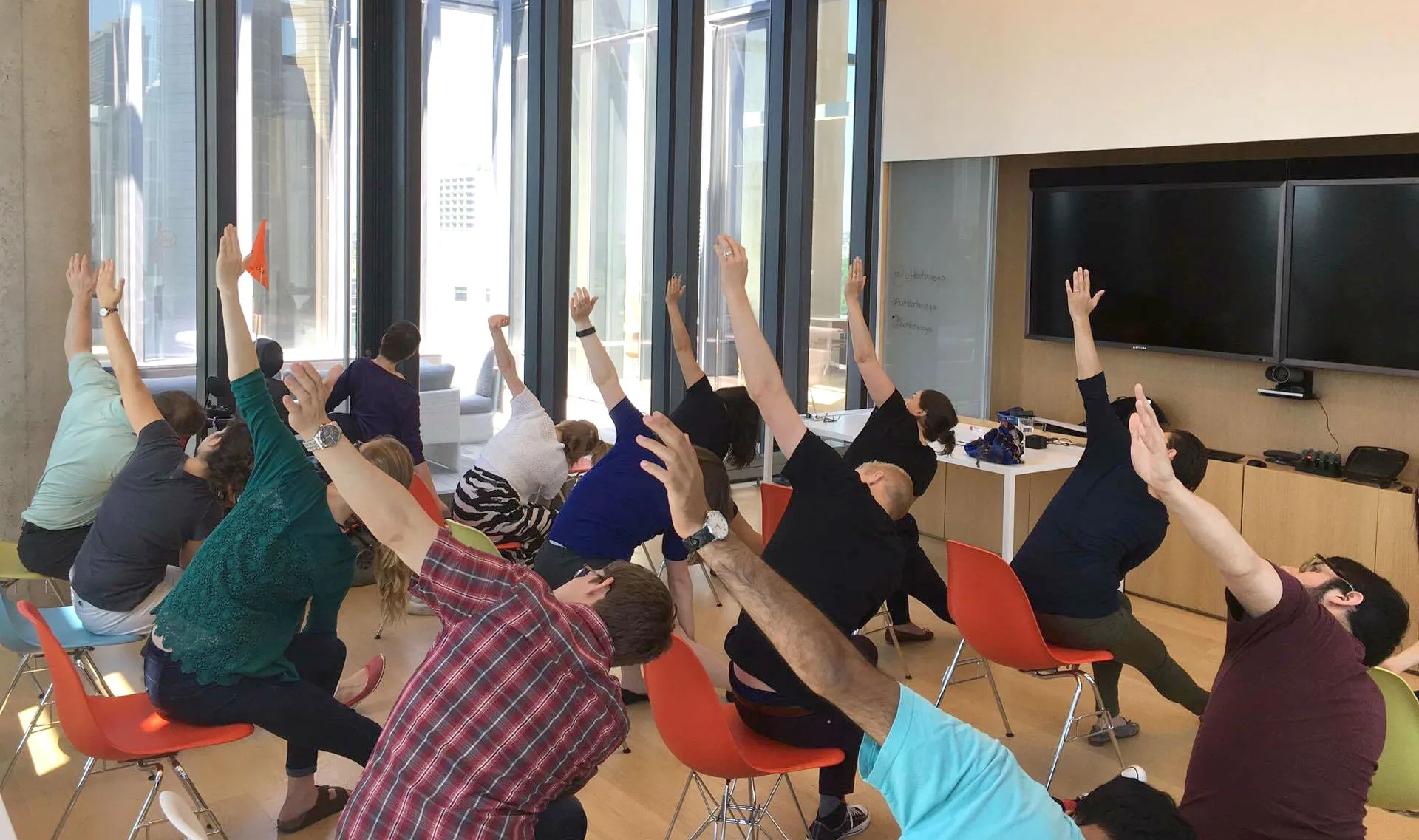 A group in everyday work clothes following a seated side stretch in a meeting room