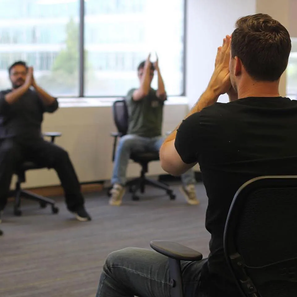 Employees following a seated stretch during an office chair yoga class