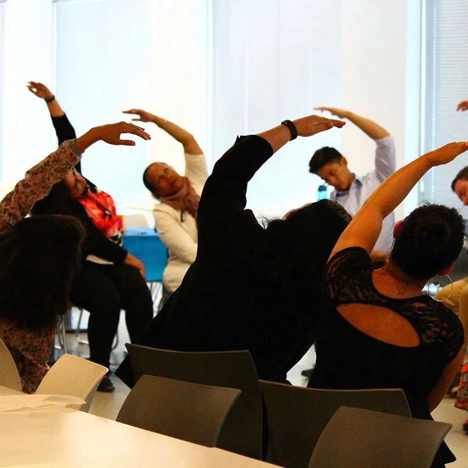 A group doing seated side stretches together in a meeting room