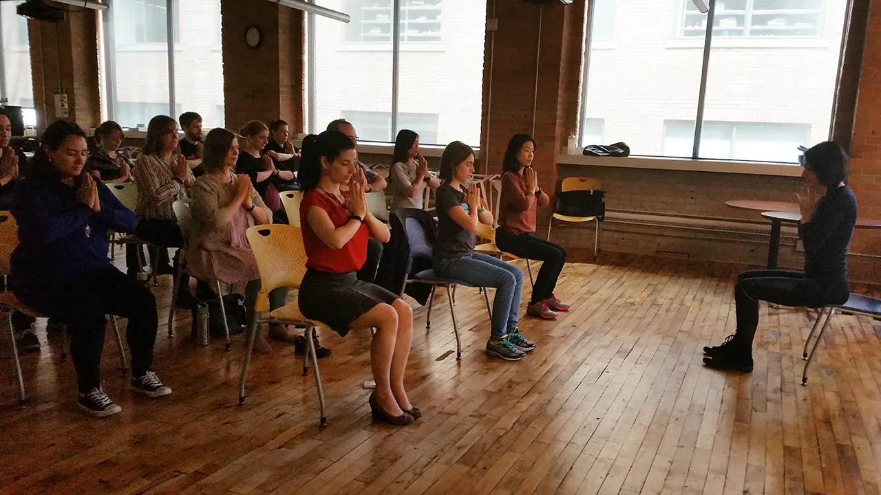 Colleagues following a seated side stretch in a bright office meeting room