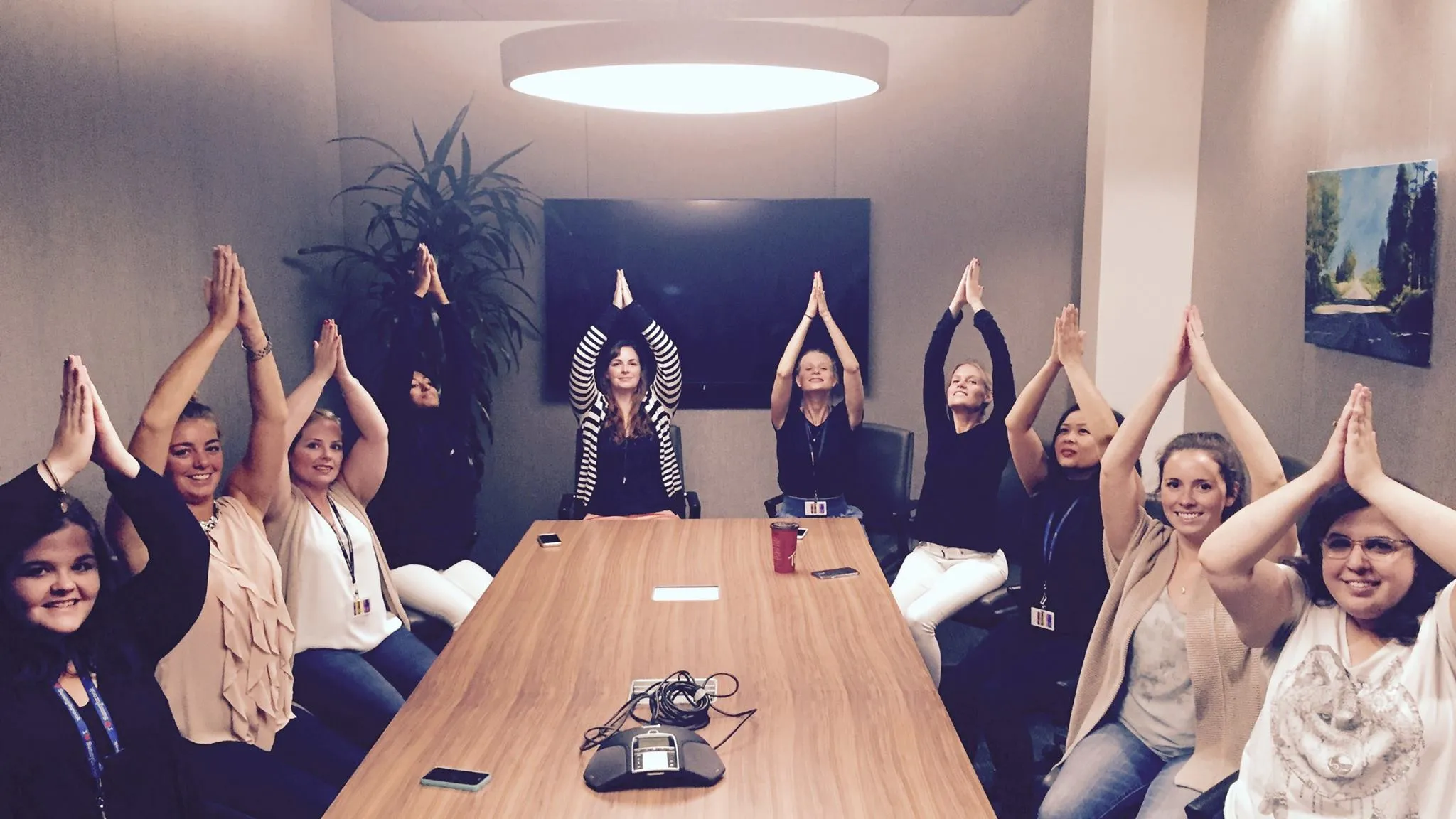 Workplace participants and a Utkata Yoga instructor stretching their arms while seated around a meeting table