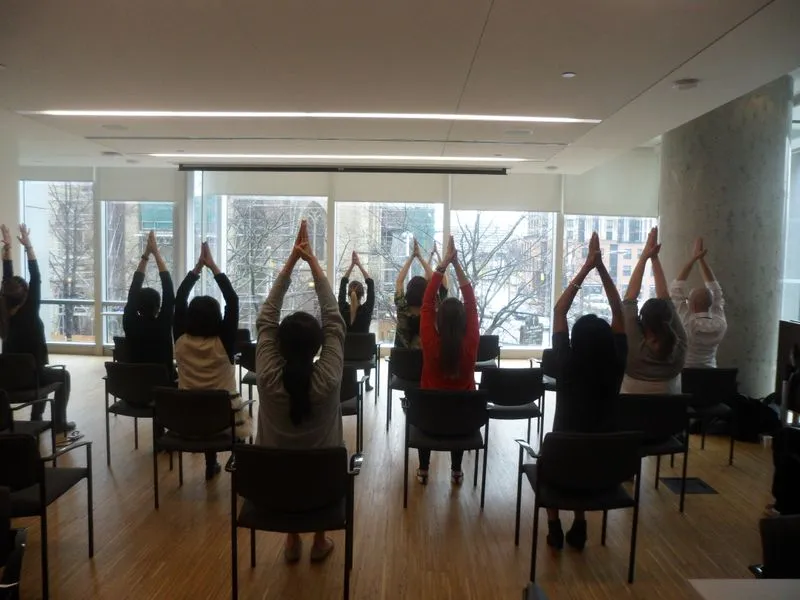 A group raising their arms during a chair yoga session in a meeting room