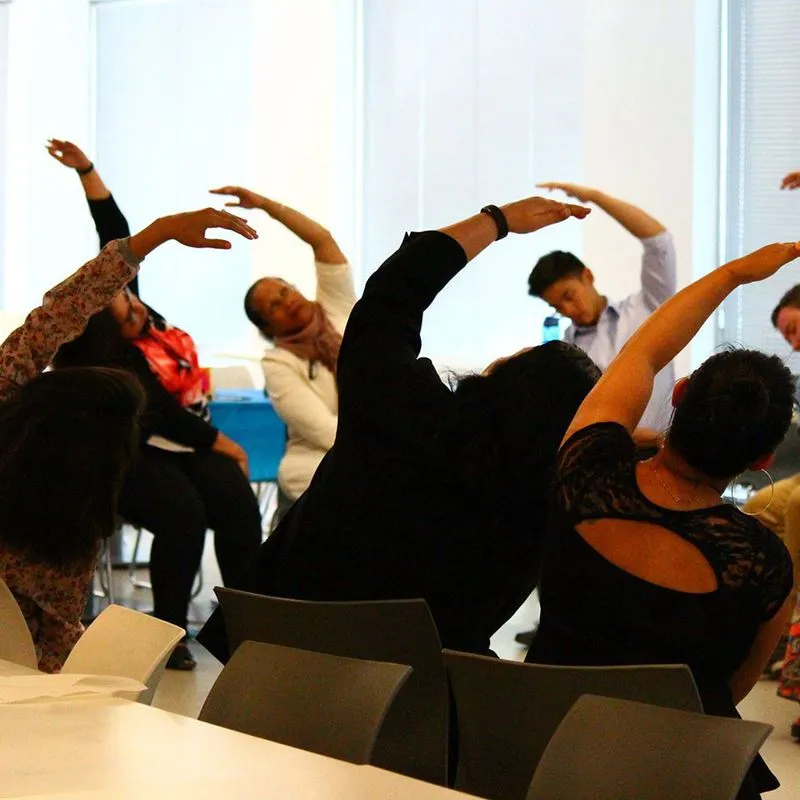 A group doing seated side stretches together in a meeting room