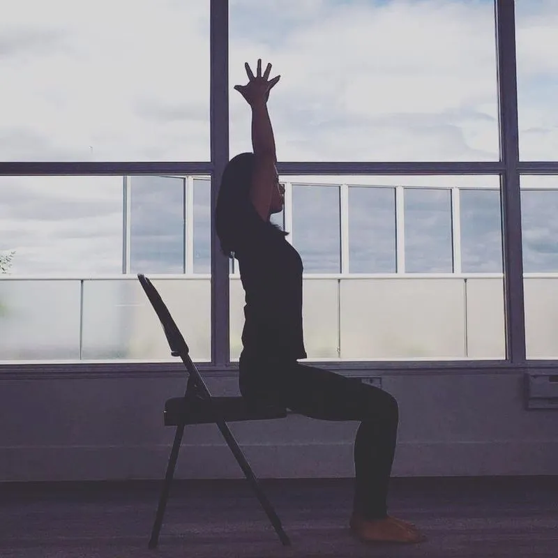 A participant stretching upward from a chair beside a window