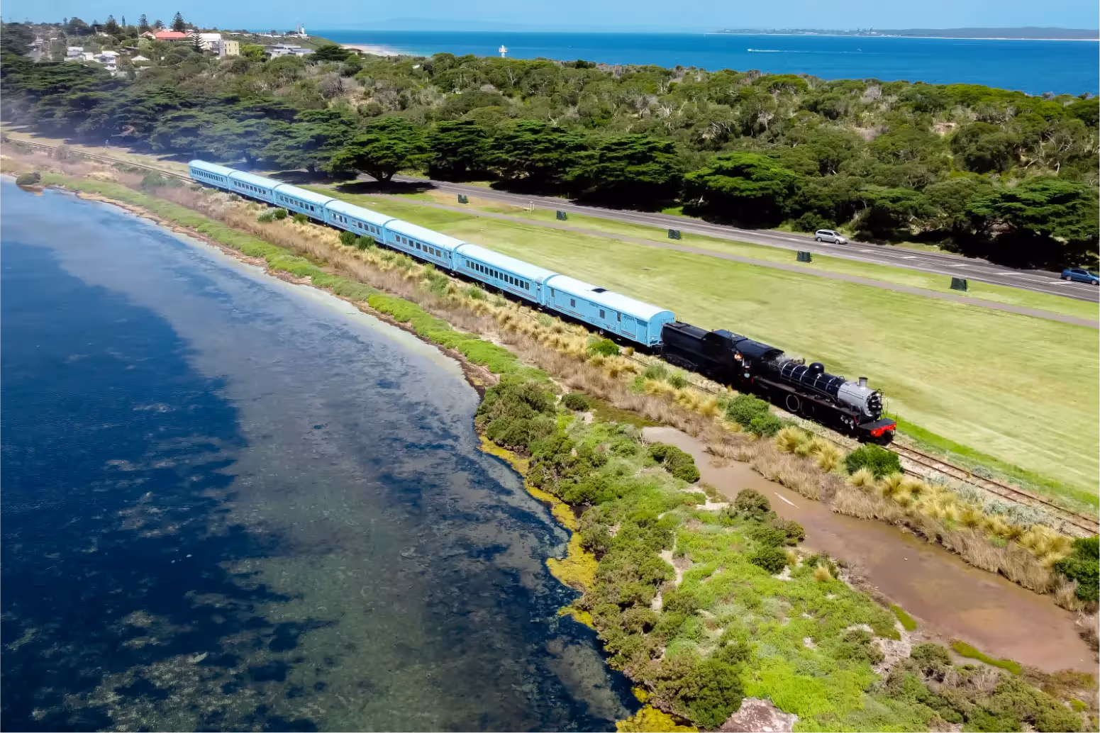 A train travelling along the coast with a beautiful green vista behind