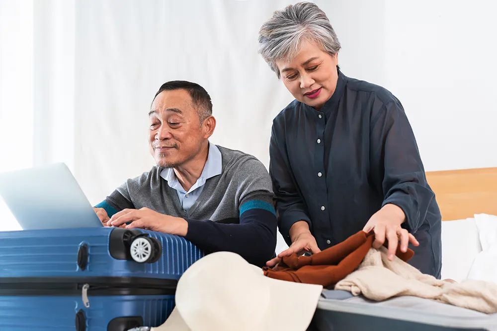 Senior couple packing efficiently for a trip, rolling clothes and using a carry-on, ready for a stress-free holiday adventure.