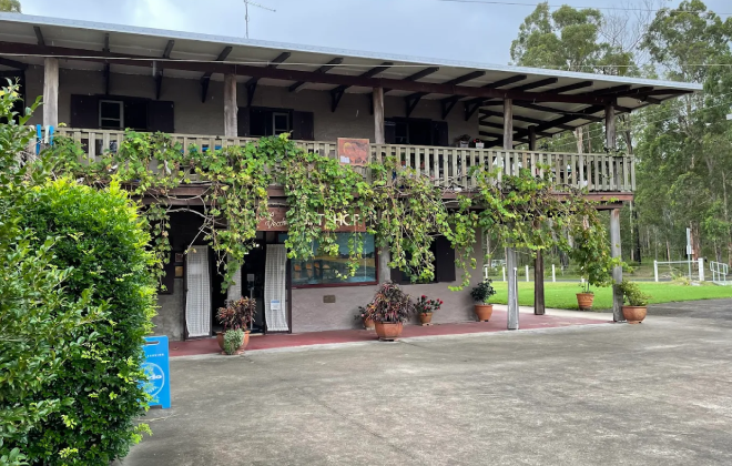 Exterior of a rustic two-storey building with a balcony and greenery at the New Italy Museum site.