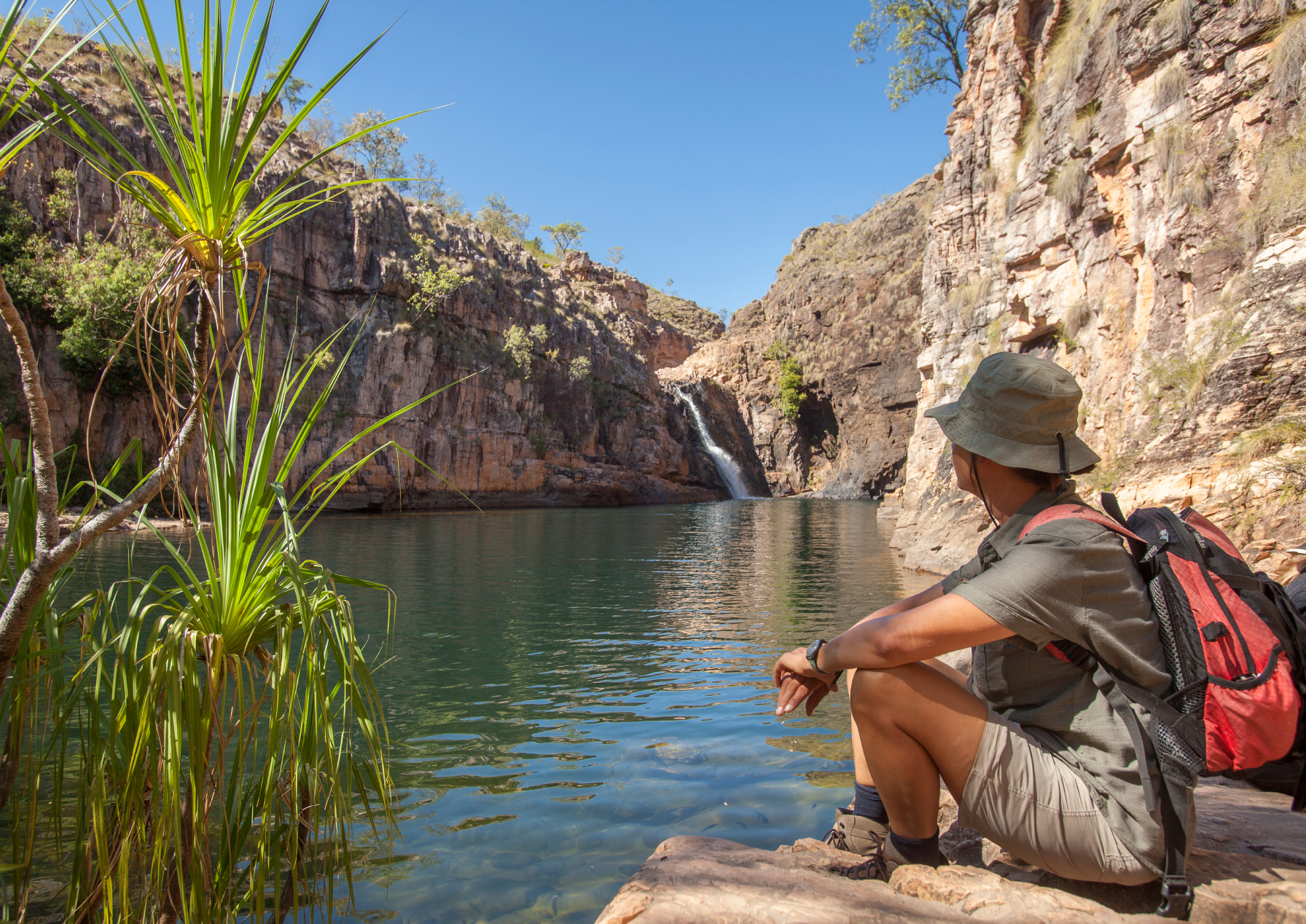 A traveller relaxing beside a serene rock pool with a waterfall at Kakadu National Park, Northern Territory.