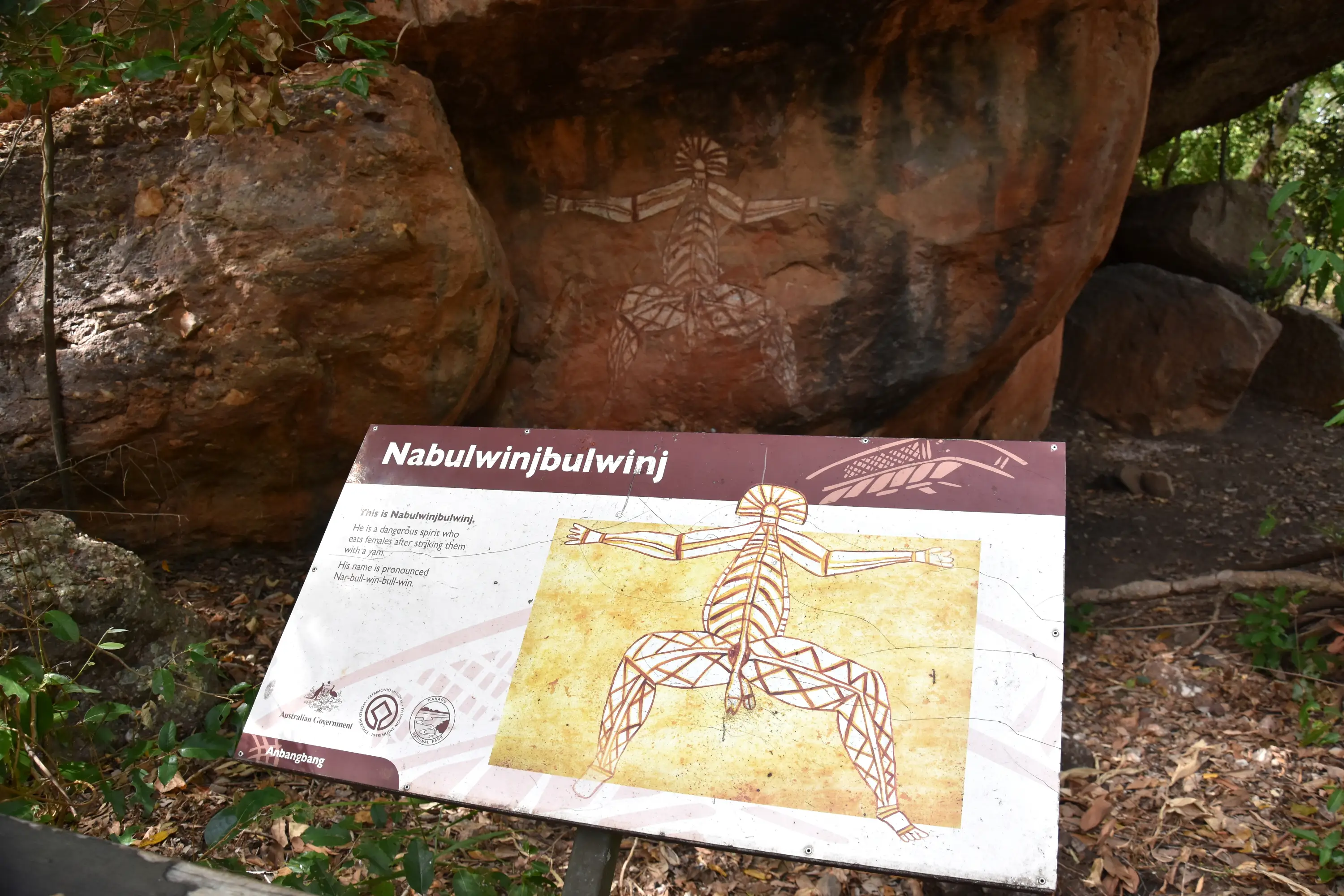 Interpretive sign and Aboriginal rock art of Nabulwinjbulwinj at Nourlangie in Kakadu National Park, showing traditional figure painting on sandstone.