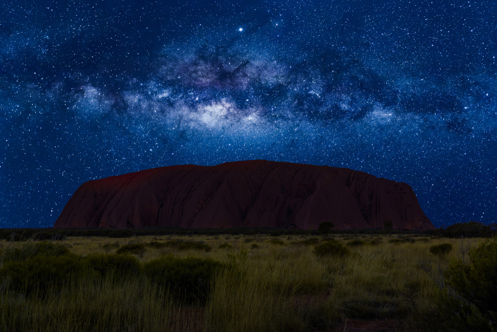 Uluru silhouetted at night beneath a star-filled sky.