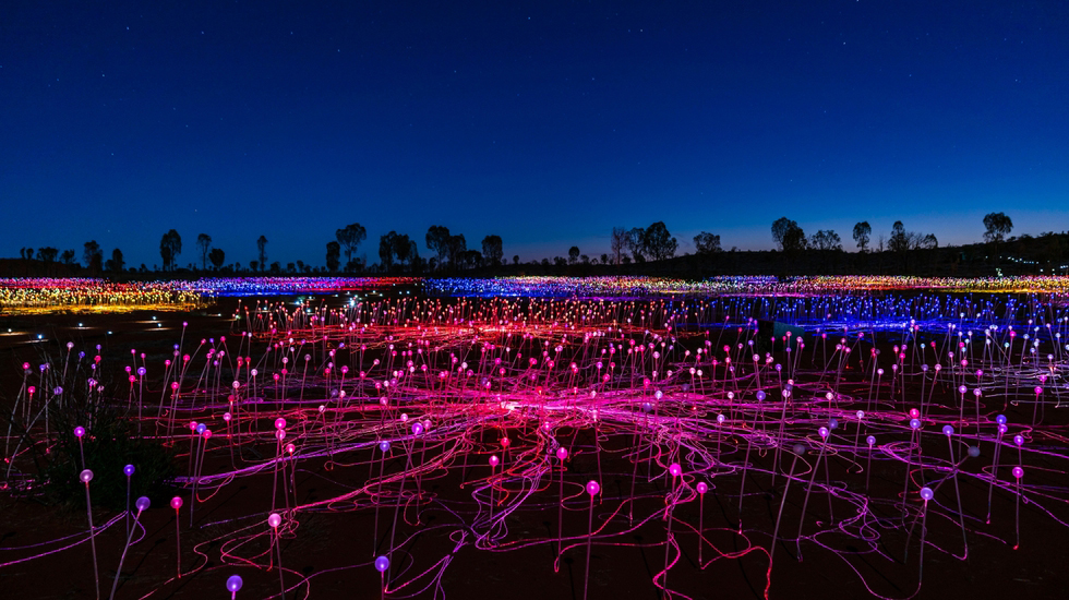 Field of Light installation at Uluru glowing in vibrant colours under a starry night sky.