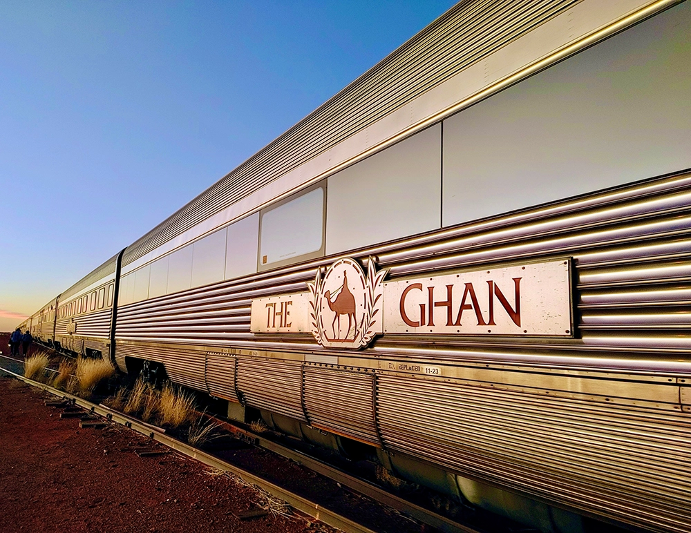 Side view of The Ghan train travelling through the Australian outback under a clear blue sky.