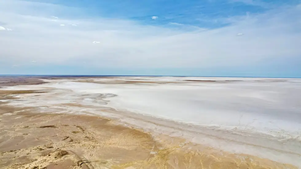 Aerial view of the salt flats and shoreline of Lake Eyre under a wide blue sky in the South Australian outback.