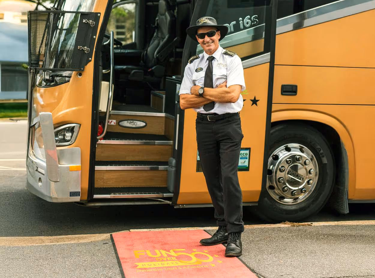 Gold Class coach driver standing at the open entrance with a Fun Over 50 Holidays welcome mat on the ground