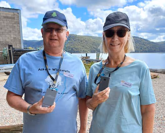 Two tour guests holding portable tour guide audio receivers during an outdoor sightseeing stop