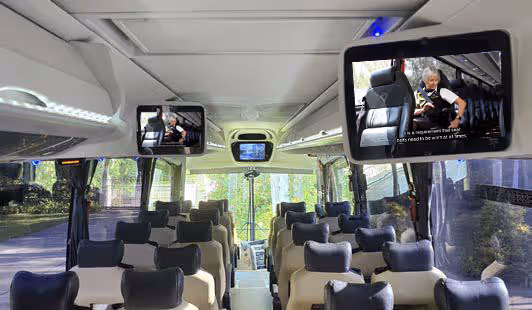 Coach interior with overhead monitors playing the onboard safety video with closed captions