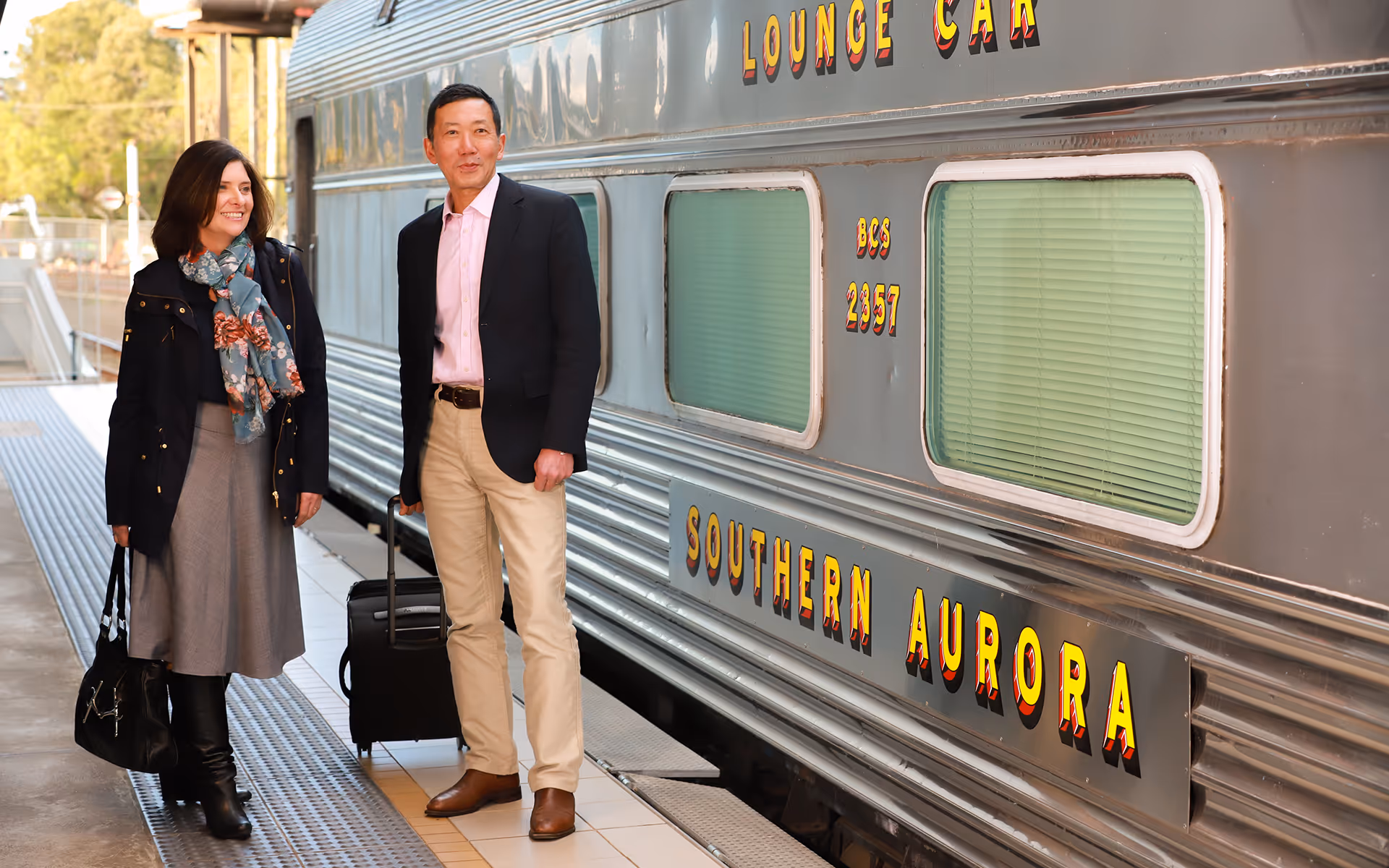 Guests with luggage standing beside the Southern Aurora lounge car at a train station