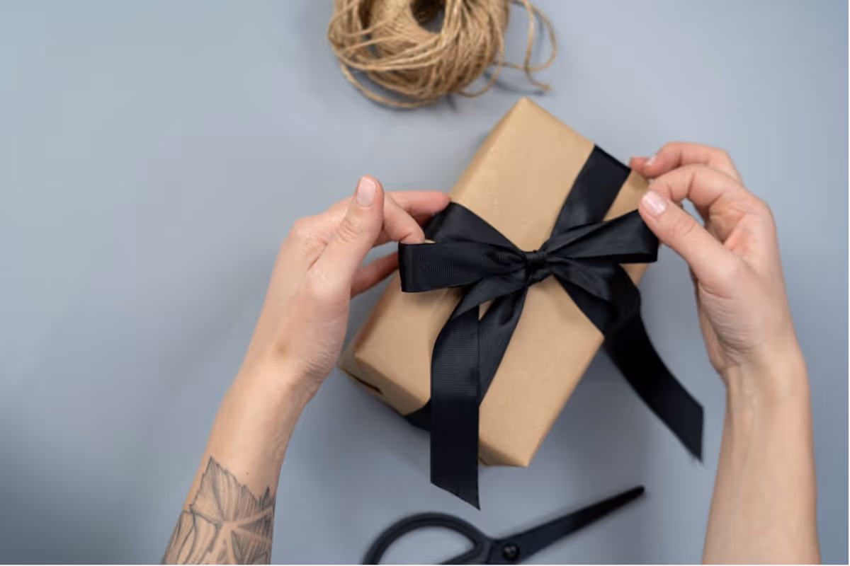 Hands wrapping a gift with beige paper and a black ribbon