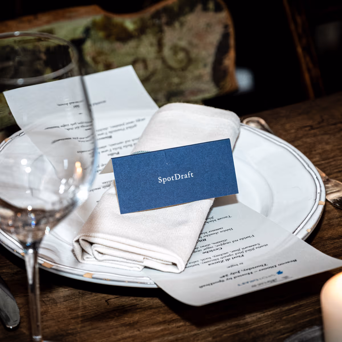 Table setting with a folded white napkin, a blue place card reading 'SpotDraft,' menus, and a wine glass.