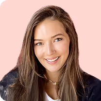 Smiling woman with long brown hair wearing a black jacket against a pink background.