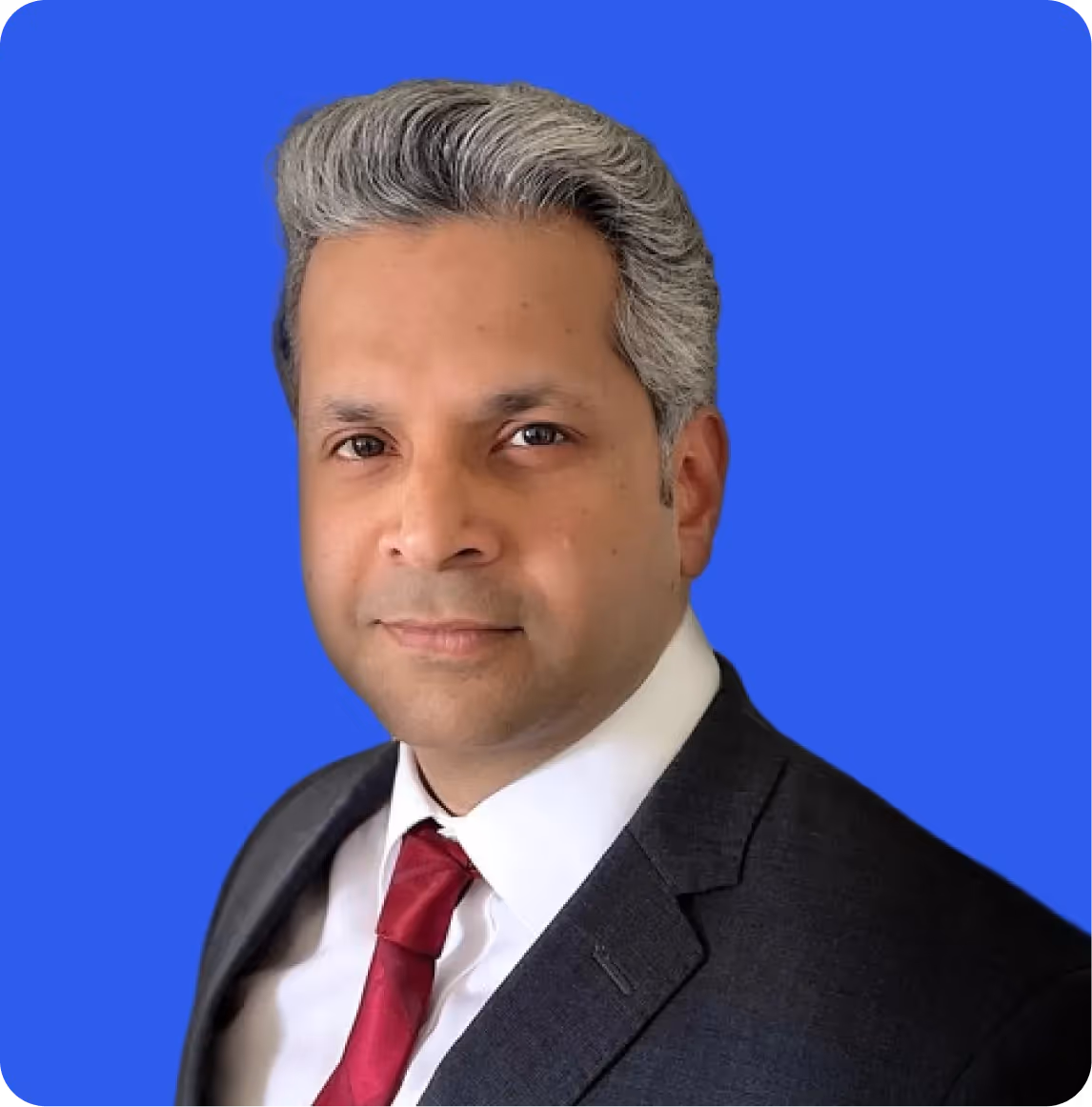 Professional headshot of a man with gray hair wearing a dark suit, white shirt, and red tie against a blue background.