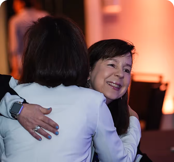 Two women hugging, one smiling warmly with a softly lit background.