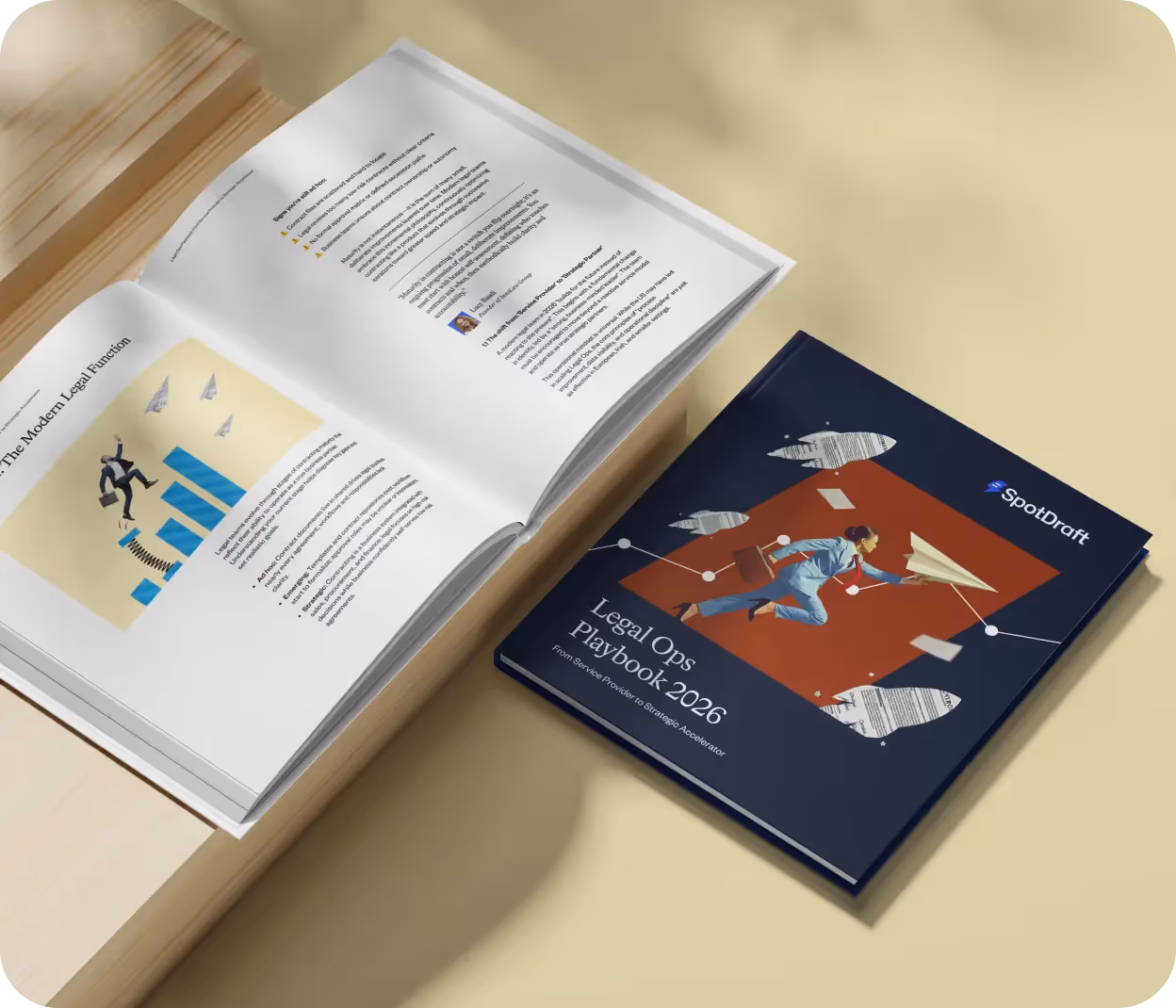 Two books on a wooden surface, one open showing pages with text and an illustration of a man jumping on bars, and the other closed with a blue cover titled 'Legal Ops Playbook 2026' featuring a running woman holding a briefcase and paper airplane.