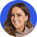 Smiling woman with wavy brown hair, wearing gold hoop earrings and a beige top, against a blue circular background.