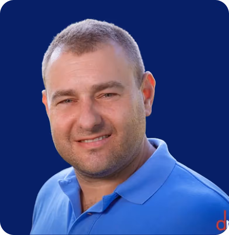 Smiling man with short hair wearing a blue polo shirt against a dark blue background.