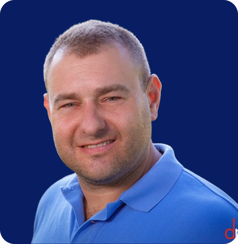 Smiling man with short hair wearing a blue polo shirt against a dark blue background.